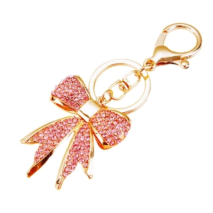 Golden metal keychain with pink rhinestone bow pendant on white background