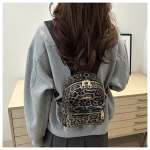 Model wearing leopard print mini backpack with golden zippers in a home setting