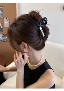 Vue détaillée d'une pince à cheveux noire mate ornée de quatre perles blanches élégantes