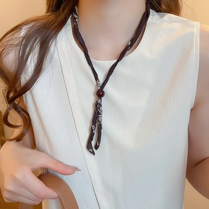 Detail of printed silk scarf necklace featuring a dark red bead on a black fabric band
