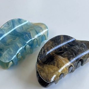 Detail view of two marble patterned hair claw clips in blue-yellow and black-gold tones