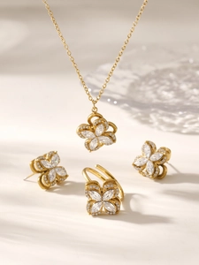 Macro detail of golden jewelry set featuring clover-shaped zircon necklace, earrings and ring