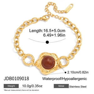 Detail of gold stainless steel bracelet with flower charm and red gemstone inlay