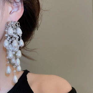 Detail view of long silver tassel earrings with white teardrop pearls on model