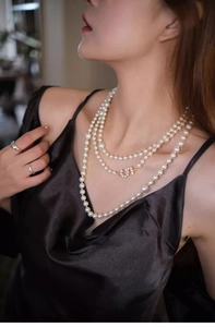 Detailed view of layered white pearl necklace with zircon number 5 on black velvet dress