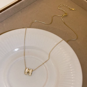 Close-up of a gold-plated H-shaped necklace with white inlay on a ceramic display