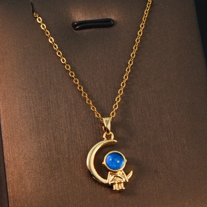 Detailed close-up of a gold moon and astronaut pendant with a blue bead on a fine chain