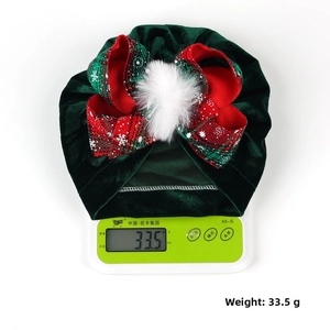 Detail view of velvet baby turban with festive plaid bow and white fur pompom weighing 33.5g