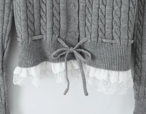 Detail of gray cable-knit cardigan featuring a drawstring bow and white lace trim hem