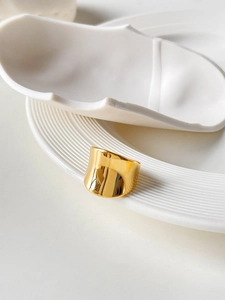 Close-up of polished 18K gold plated wide titanium steel ring on minimalist white background