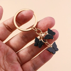 Close-up of three black acrylic butterflies on a gold keychain held in hand