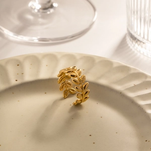Detailed macro shot of a golden olive branch ring on a ceramic tray with warm lighting