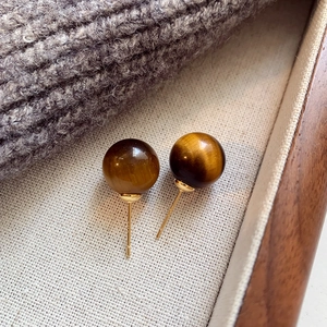 Macro shot of tiger eye stone bead earrings with golden pins on a cozy knit fabric background