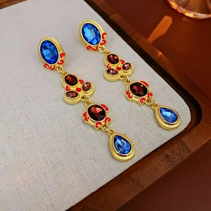 Macro view of vintage gold earrings with blue and red gemstones on a light fabric