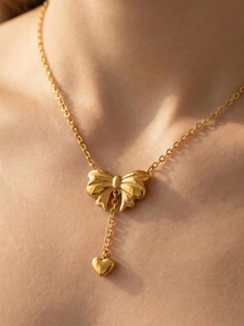 Close-up of golden necklace with 3D bow and heart pendant on a female model