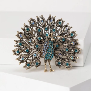 Detailed close-up of a vintage peacock brooch with blue rhinestones on a white background