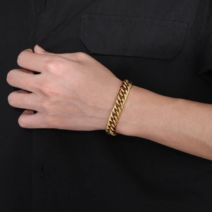 Polished golden Cuban link chain bracelet worn on wrist by model in black shirt