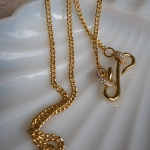 Detailed view of a gold snake pendant necklace with shimmering zircon stones on a shell tray