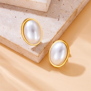 Elegant gold oval stud earrings with large white pearls set on a textured marble background