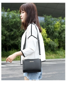 Outdoor view of a black pebble leather crossbody bag with white stitching and gold logo