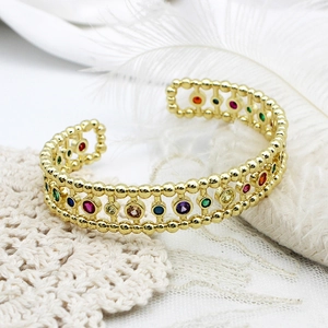Macro view of adjustable gold bangle with multi-color zircon stones on white lace