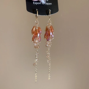 Macro detail of bohemian amber crystal drop earrings with delicate long gold chain tassels