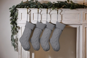 Detail of four grey cable knit Christmas stockings hanging on a rustic white mantelpiece