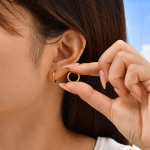 Close-up of minimalist gold huggie hoop earrings worn by a model in outdoor lighting