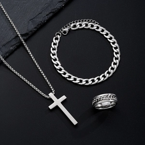 Flat lay of men's stainless steel cross necklace, cuban bracelet, and spinner ring set