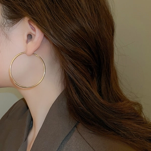 Close-up of a large minimalist gold hoop earring worn by a model in a side view