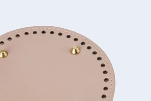 Macro view of a round light pink leather bag base with golden metal studs and pre-punched holes