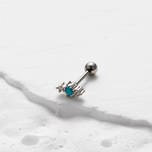 Detail of silver cartilage stud featuring a turquoise stone on a white stone surface