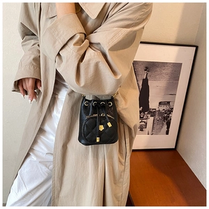 Detail of a mini black quilted bucket bag with a golden camellia flower charm and drawstring