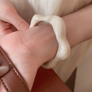 Detail view of wavy cream resin bangle on wrist with smooth glossy finish