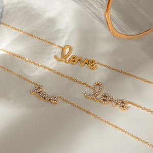 Three gold stainless steel Love letter necklaces with rhinestones on white fabric
