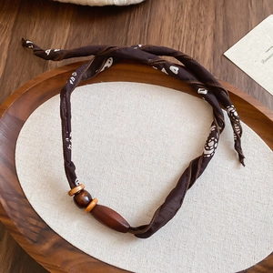 Detail of brown paisley fabric necktie necklace with natural wooden beads on a tray