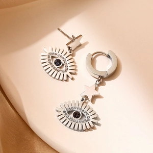 Silver star and evil eye drop earrings with sparkling rhinestones on beige fabric