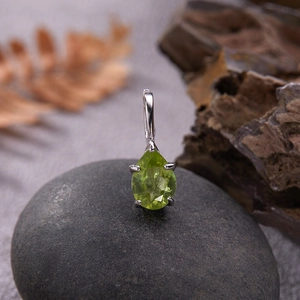 Macro shot of S925 silver pendant with pear-cut green gemstone on a dark pebble stone