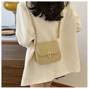 Detail of woven beige shoulder bag featuring a gold horseshoe buckle and leather strap