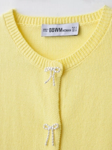 Close-up of yellow knit cardigan showing pearl bow buttons and neckline brand label