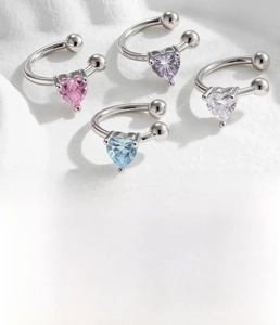 Detail of heart-shaped zircon ear cuffs in pink, purple, white, and blue on stone surface