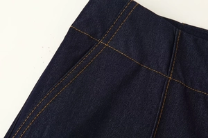 Détail d'une veste en jean bleu foncé avec double surpiqûre orange contrastée et finitions