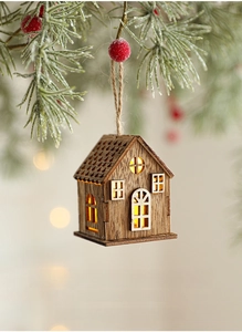 Dettaglio di casetta di Natale in legno con LED appesa a rami di pino decorati