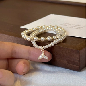 Detail view of a double-layered pearl bracelet with a sparkling zircon fishtail pendant