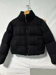Detail of black knitted jacket featuring textured cable patterns and a high stand collar