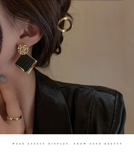 Detail of gold textured round stud earring with black square drop charm on model