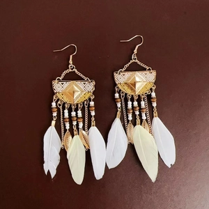 Detailed close-up of bohemian earrings with golden leaves and soft white feathers