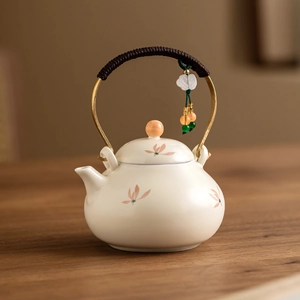 Elegant beige ceramic teapot with orchid pattern and woven rope handle on wooden table