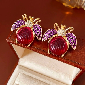 Detail of vintage bee stud earrings with red gemstone, purple enamel, and crystals