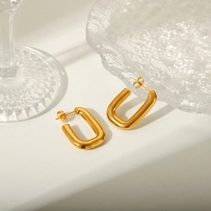 Close-up of gold U-shaped geometric earrings displayed on textured clear glassware